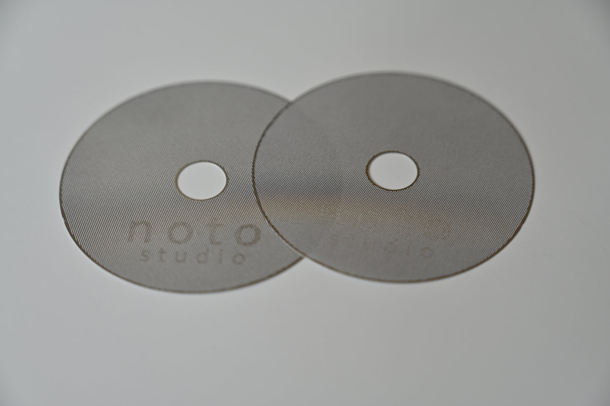 Two noto studio 316L stainless steel puck screens on a white background, one laser-etched with the noto studio logo