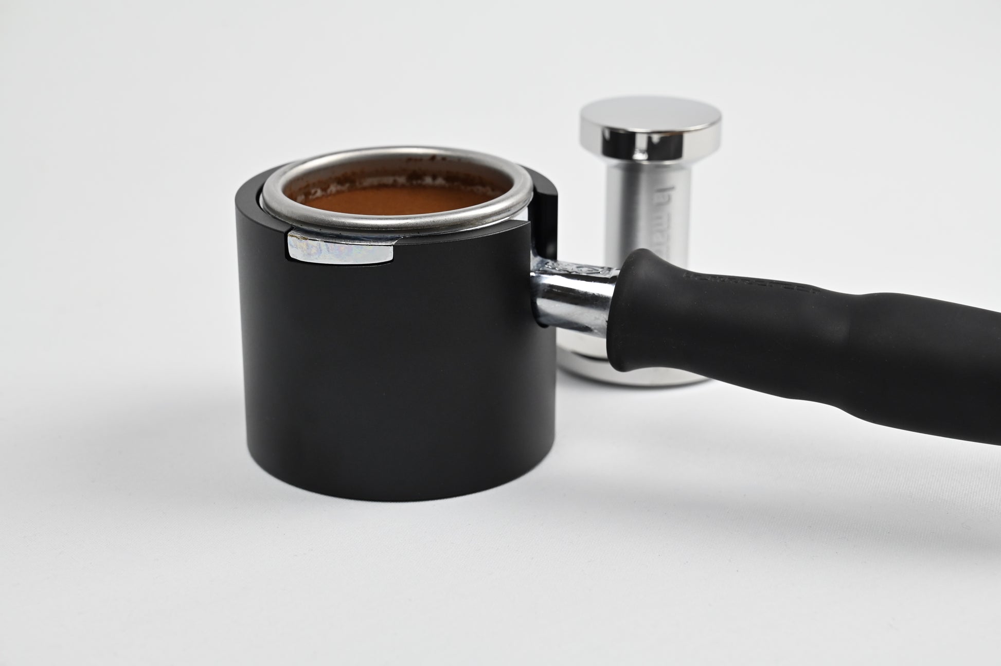 La Marzocco portafilter seated in the black noto studio tamper station with a tamper